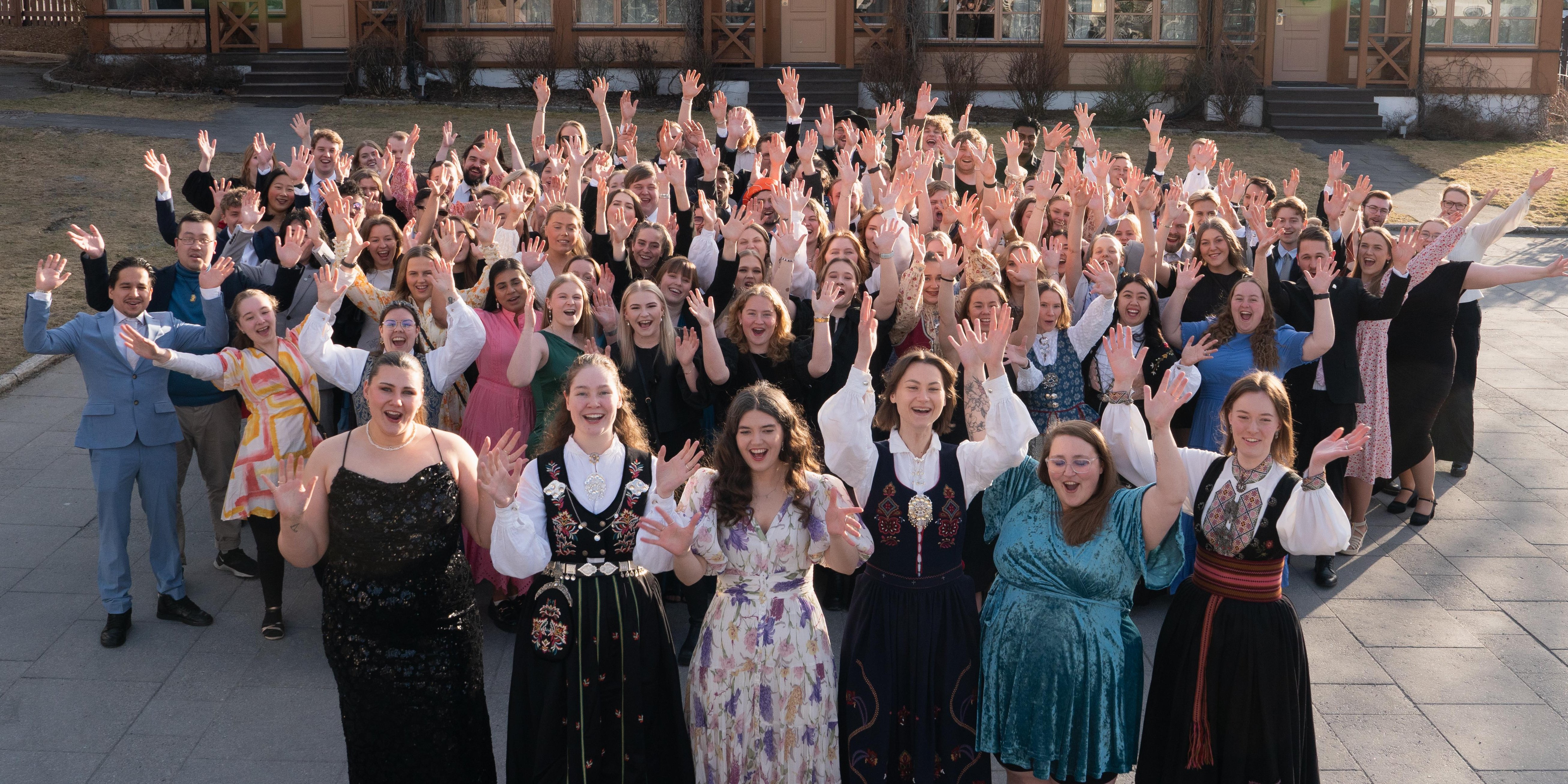 Stor gjeng med festkledde studenter i både bunad og dress.