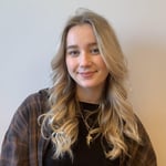 Ung kvinne i 20-årene med blondt hår smiler til kamera foran hvit vegg