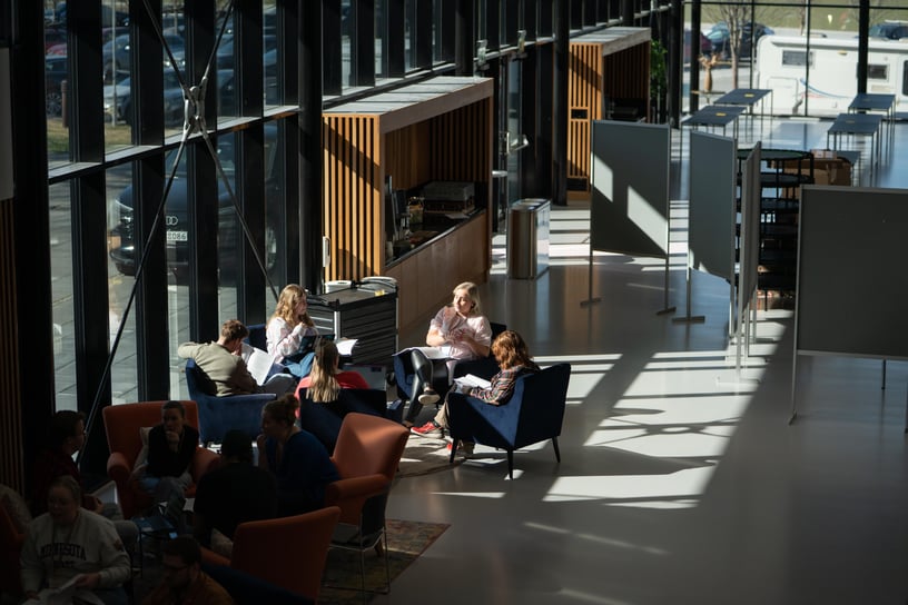 Bilde av et konferanserom. I midten sitter en gruppe mennesker og snakker sammen.