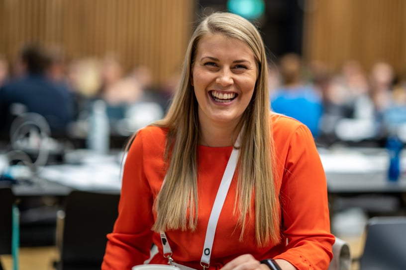 En blid kvinne i 20-årene med langt lyst hår og oransje topp.