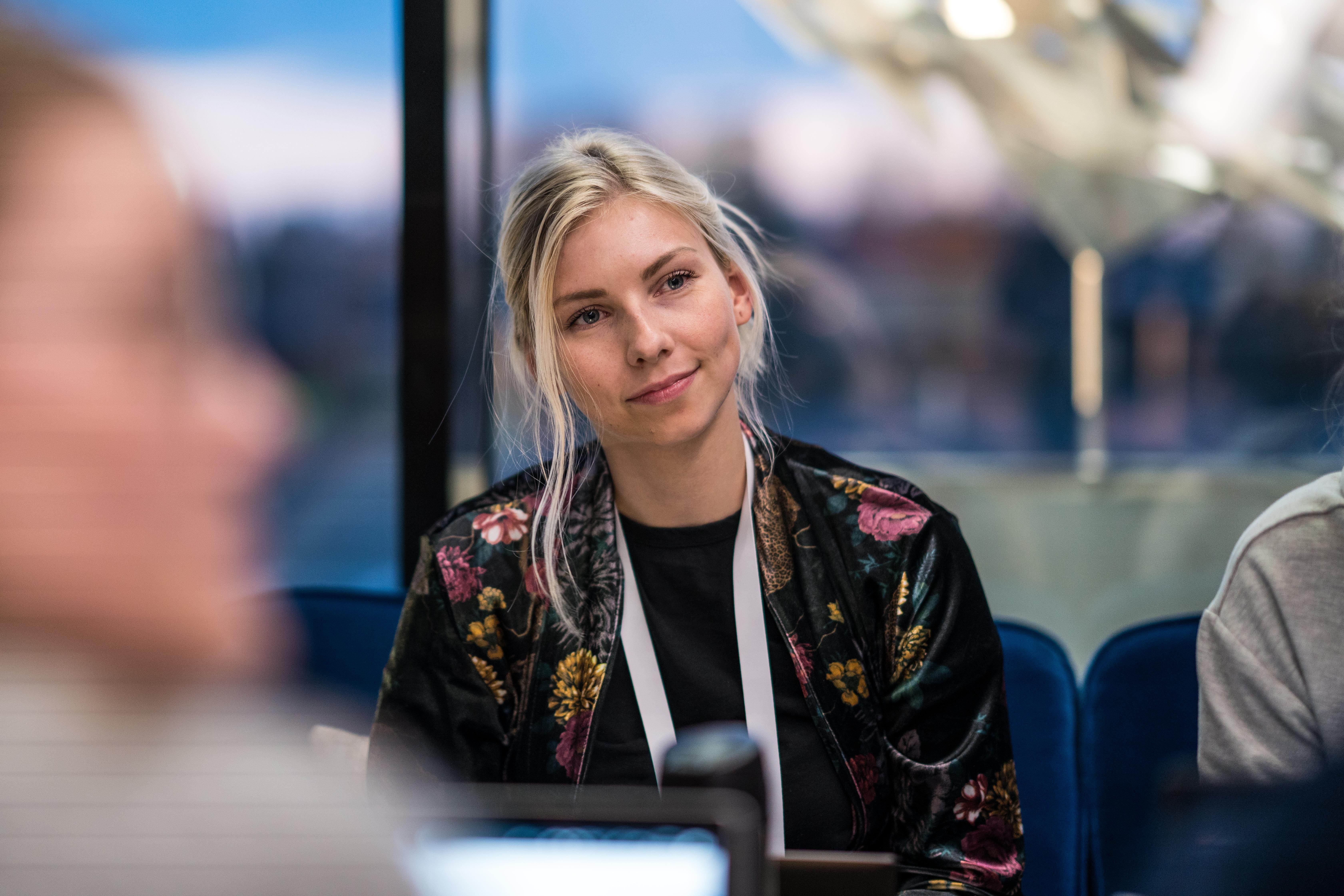 En kvinne ser smilende ut i et rom, med kroppen vendt bort fra et vindu. Foto.